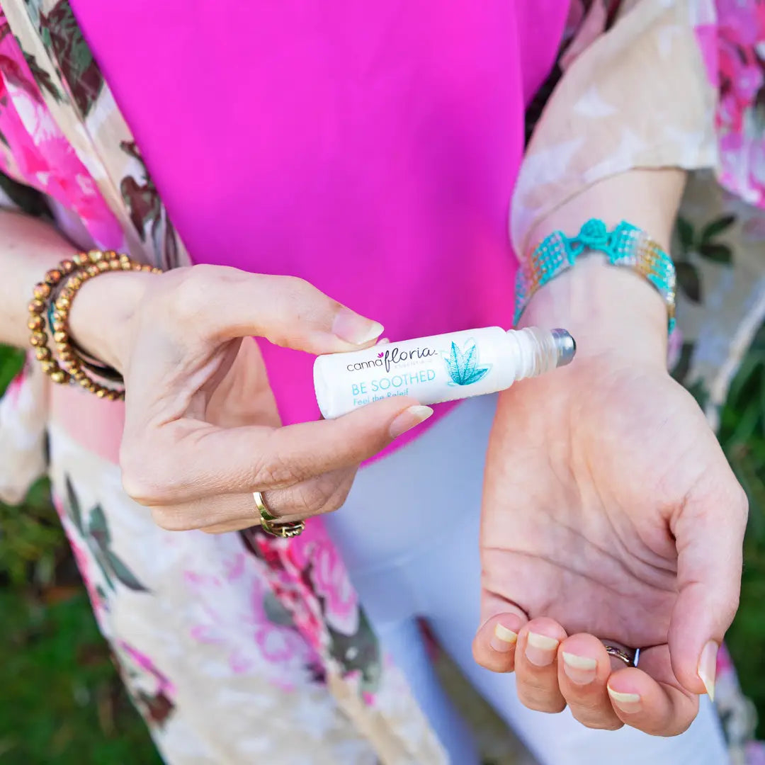 Person applying a white roll on labeled be soothed to their wrist outdoors.