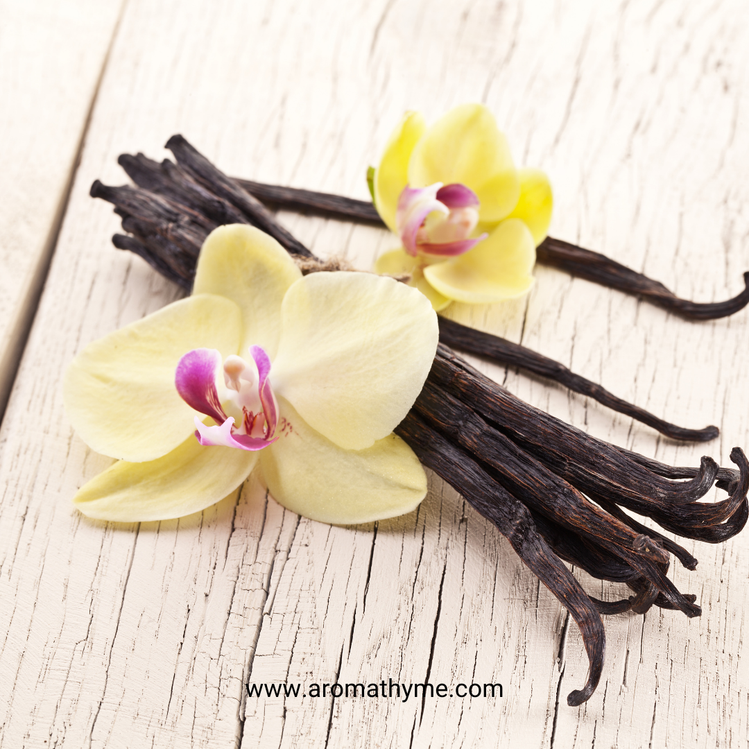 Vanilla beans with orchid flowers on a wooden surface, featuring the brand 'aromathyme'.